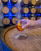 Hollywood Distillery coaster on a barrel head with a cocktail in the barrel room