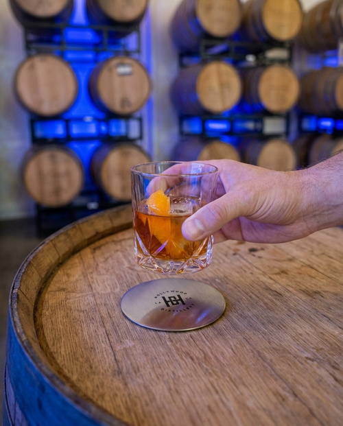 Hollywood Distillery coaster on a barrel head with a cocktail in the barrel room